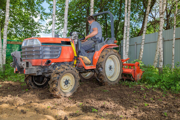A farmer on a mini tractor loosens the soil for the lawn. Land cultivation, surface leveling.