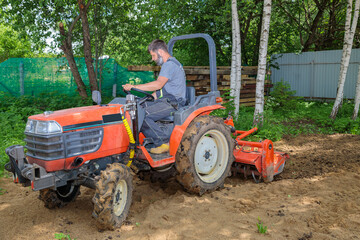 Obraz premium A farmer on a mini tractor loosens the soil for the lawn. Land cultivation, surface leveling.
