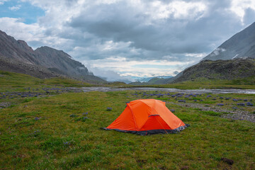Scenic mountain landscape with tent in rain drops in sunlight under cloudy sky. Dramatic alpine...