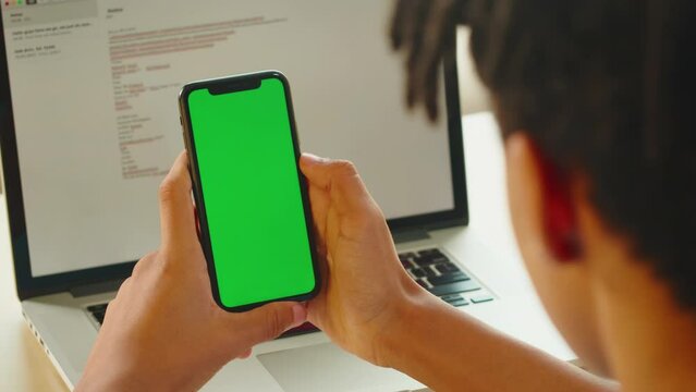 African American man using smartphone with chroma key close-up. Young guy holding mobile phone with green screen, teenager surfing the internet, watching video. 