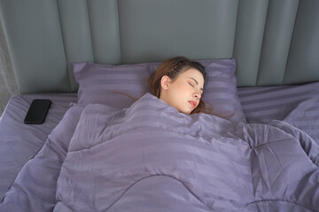 Woman sleeping on the bed in morning and trying to turning off or snoozing the alarm clock.