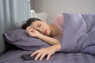 Woman sleeping on the bed in morning and trying to turning off or snoozing the alarm clock.