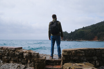 person from behind on the top of the rocky mountain watching around at the sea storm. achievement, freedom and win concept. out of the city, relaxation and place of power