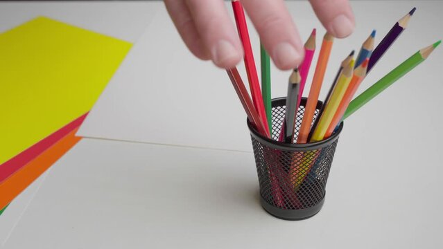 The artist takes a colored pencil from a stand. Close-up hand takes a black pencil from a set of pencils.