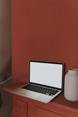 Laptop computer with blank screen, clay pots against red color wall. Aesthetic template with mockup copy space. Online store, blog, social media, website branding. Online shopping concept