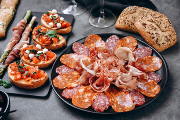 Food antipasto prosciutto ham, salami, olives and  bread sticks. cheese on a board parmesan, pecorino, gorgonzola. Tomato and basil bruschetta. Two glasses of white wine or prosecco