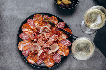 Salami on a black plate and olives and  r white wine or Prosecco in a restaurant aperitif meal