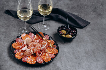 Salami on a black plate and olives and  r white wine or Prosecco in a restaurant aperitif meal