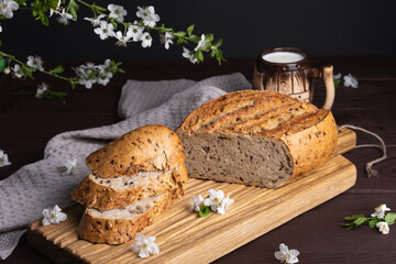 Pieces of fresh homemade rye bread with clay mug of milk on wooden cutting board. Healthy breakfast