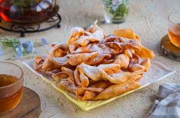 Deep fried brushwood cookies or angel wings on a square white plate on a light concrete background. Deep-fried baking.