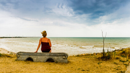 a woman sitting on the bench and looking at the sea