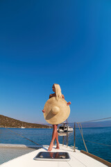 Beautiful young blond woman in bikini standing on catamaran bow at sunny summer day