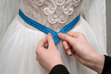close up of female designer hand fitting bridal dress with measure tape in  boutique