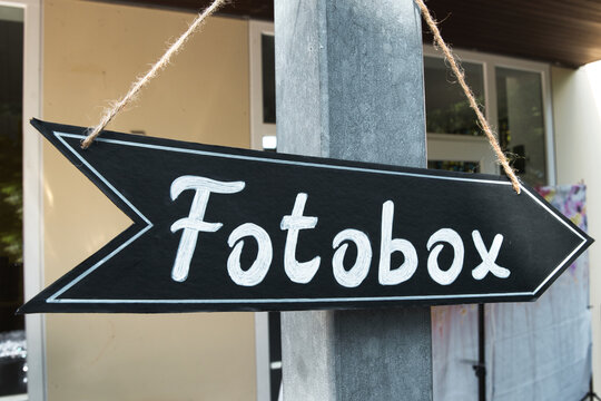 Sign giving directions and saying 'Fotobox' in german language which translates to photobooth in English. Party equipment, wedding party, photography equipment.  