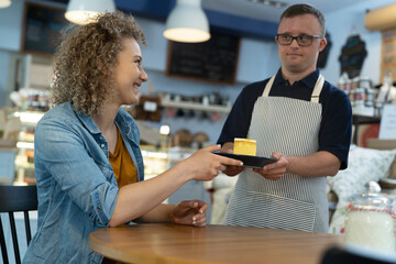 Caucasian man with down syndrome serving a piece of cake in the cafe