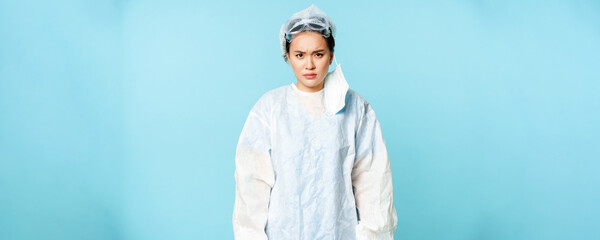 Angry asian woman doctor or nurse, wearing personal protective equipment, looking with disapproval,...