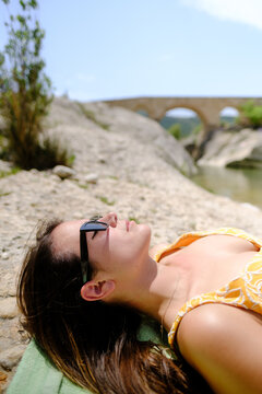 Young pretty caucasian woman sunbathing on the rocks close to the river