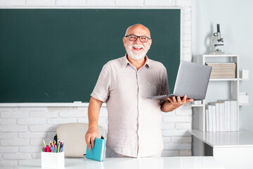 Portrait of mature teacher or tutor professor working at table in college or high school. Elderly education and retired knowledge concept. - obrazy, fototapety, plakaty