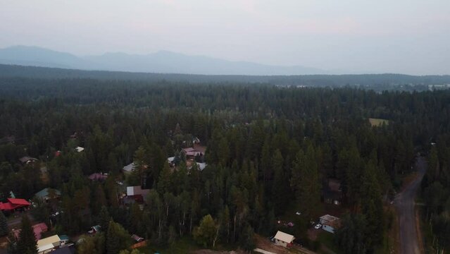 Clockwise drone shot of the forest on a smoky day in a small town in Idaho. This 4K cinematic shot, which features hazy mountains in the background, was filmed using a DJI mini 2 drone.