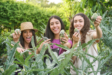 Portrait of three female farmers holding artichokes smiling and looking at camera in an urban...