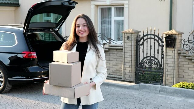 Young business woman picking up parcels from a car trunk, coming home by car. Concept of buying goods online and delivering them home