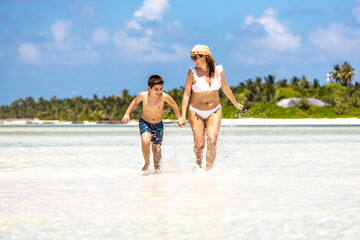 Mother and son running through the water on a white sand beach