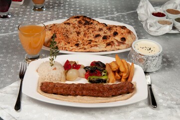 Shish kebab is made of lamb. There is shish kebab, pita bread and fruit juice on the dining table.