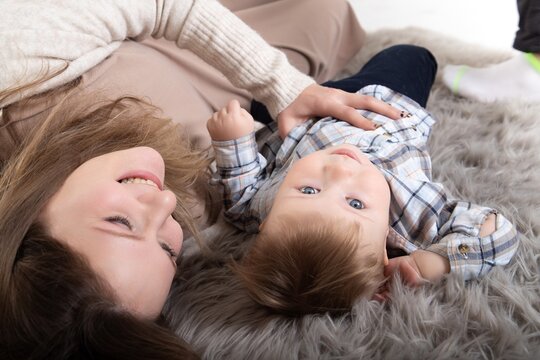 A young caucasian woman with her toddler lie on a floor and have fun together.