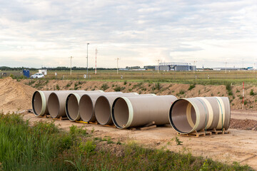 Stack of big frp composite fiberglass plastic sewage pipes at warehouse construction site near Leipzig Halle airport against blue sky background. Highway road construction infrastructure earthworks