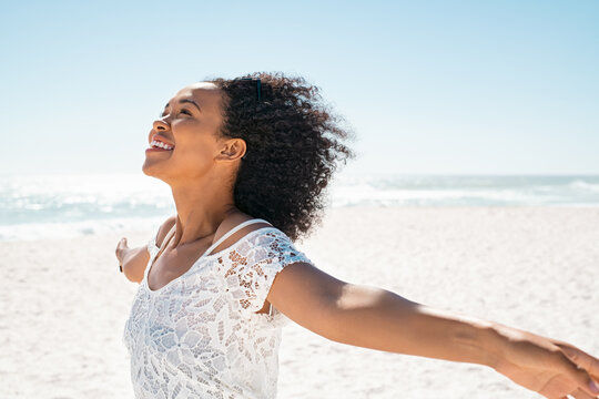 Carefree smiling black woman at beach outstretching arms