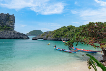 Thailand - Angthong Islands National Marine Park, view of Koh Sam Sao island with arch stone curve bridge. Long tails on calm turquoise sea by the beach, with lush foliage.