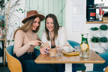 woman friends on coffee break talking and using smartphone