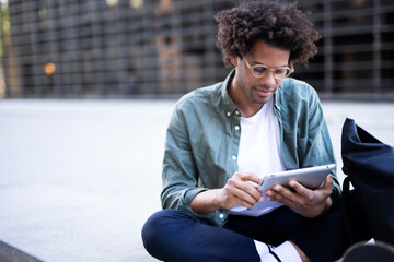 Young man with curly hair using digital tablet. Man sitting outside taking a break