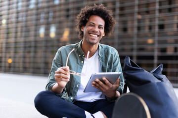 Young man with curly hair using digital tablet. Man sitting outside taking a break