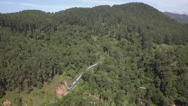 Aerial: Passenger train winds along green forested mountainside track