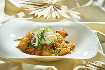 Fried potatoes with a poached egg in a plate on a white tablecloth.