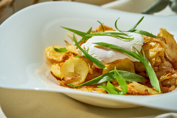 Fried potatoes with a poached egg in a plate on a white tablecloth.