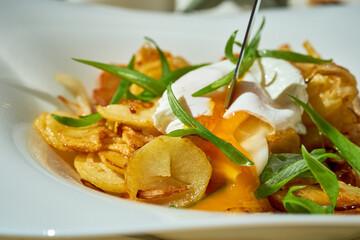 Fried potatoes with a poached egg in a plate on a white tablecloth.