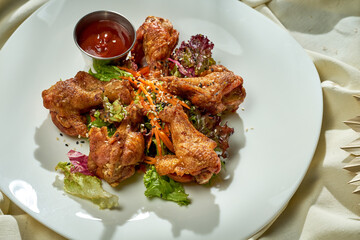 BBQ chicken wings with sauce and salad in a plate on a white tablecloth.