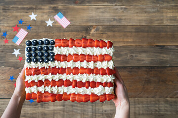 Hand serving cake with US flag colors on wooden background with decoration. Independence Day...