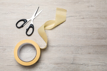 Roll of adhesive tape and scissors on wooden background, flat lay. Space for text