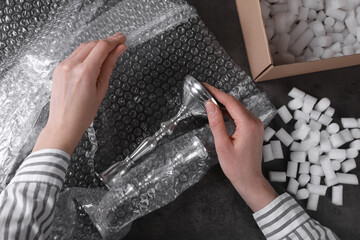 Woman covering silver candlesticks with bubble wrap at dark grey table, closeup - obrazy, fototapety, plakaty