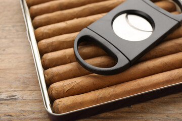 Box of cigars and guillotine cutter on wooden table, closeup