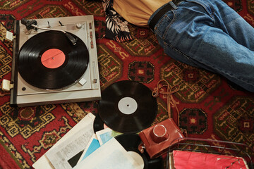 Part of young man in blue jeans relaxing on red carpet on the floor and listening to vynil disks...