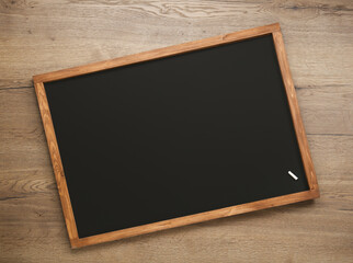 Clean blackboard with piece of chalk on wooden background, top view