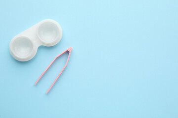 Case with contact lenses and tweezers on light blue background, flat lay . Space for text