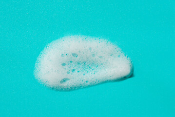 Foam swatch on a blue background. Soapy liquid texture with bubbles. Natural sunshine and shadows. Skin care cleansing cosmetic in top view.