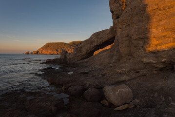 Rocky shore on the Mediterranean at sunrise with rocky arch