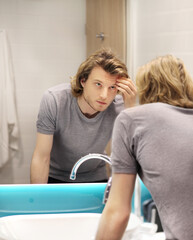Obraz premium young man looking in the mirror,combing his hair,looking at problems on face.