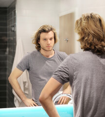 young man looking in the mirror,combing his hair,looking at problems on face.